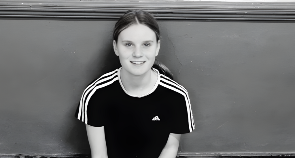 A black and white photo of Holly Newton wearing a T-shirt and smiling at the camera