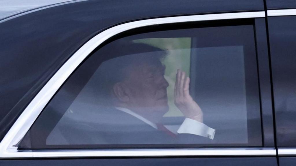 Trump holds his hand up in the car. 