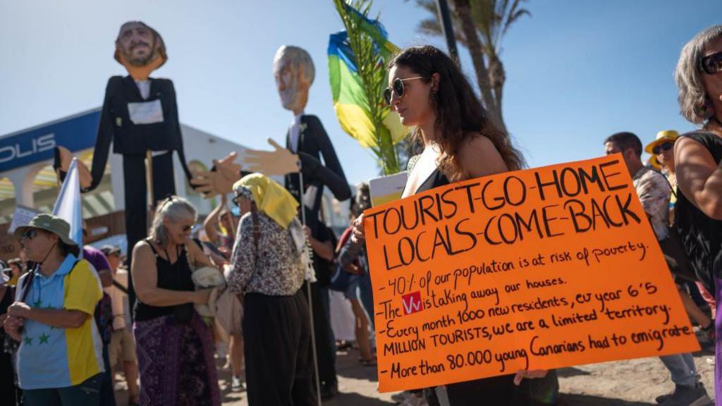 A  woman holds a sign saying "tourists go home locals come back" during a protest in Tenerife, Canary Islands