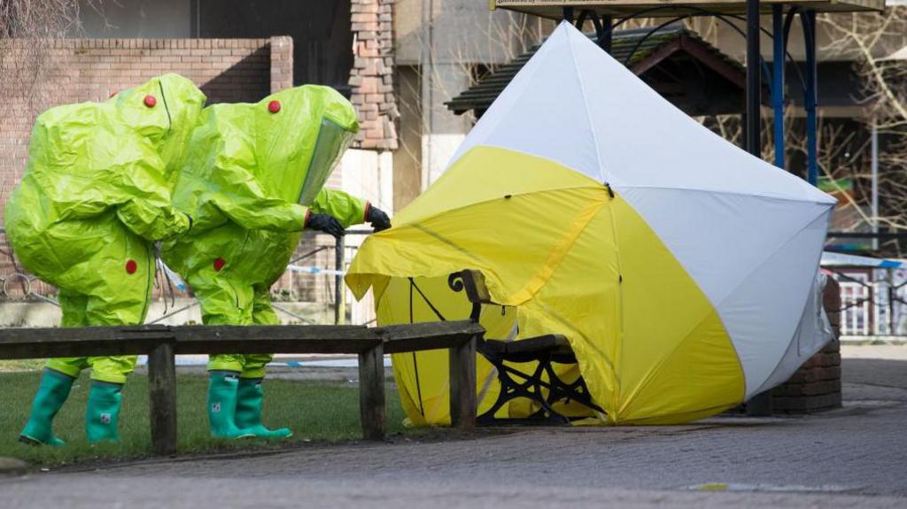 Specialist officers in lime green protective suits secure a police forensic tent covering the bench where Sergei and Yulia Skripal were found on 4 March 2018