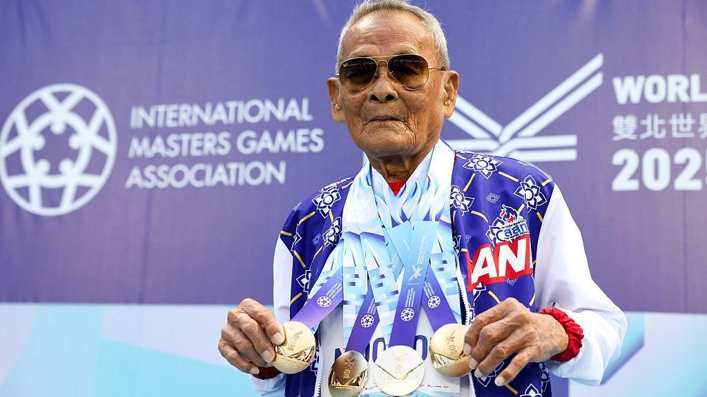 Sawang Janpram wears sunglasses as he shows off the four gold medals hanging around his neck
