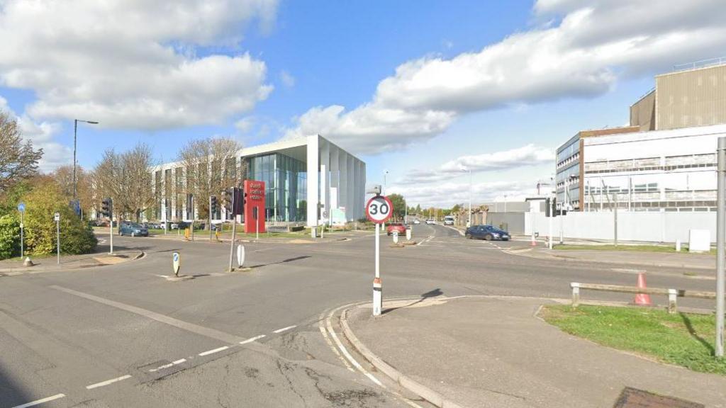 A Google Street View of a junction between a service road and a main road. Across the road a modern sign on a red horizontal block marks the entrance to Slough Trading Estate.