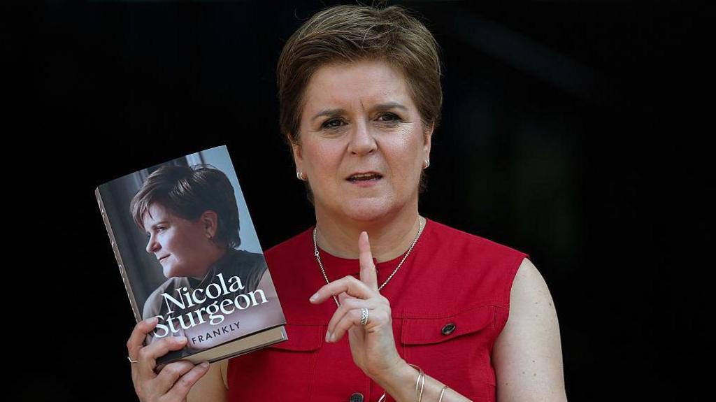 Former first minister Nicola Sturgeon (a middle aged woman with short brown hair, wearing a red top and holding up a book) pictured at the launch of her autobiography