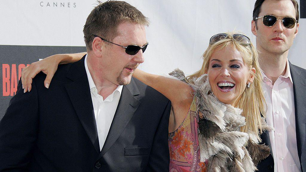 US actress Sharon Stone poses with British director Michael Caton-Jones and actor David Morrissey for their film Basic Instinct 2, the men in suits and open shirts, Ms Stone in a pink patterned dress and a feather scarf.