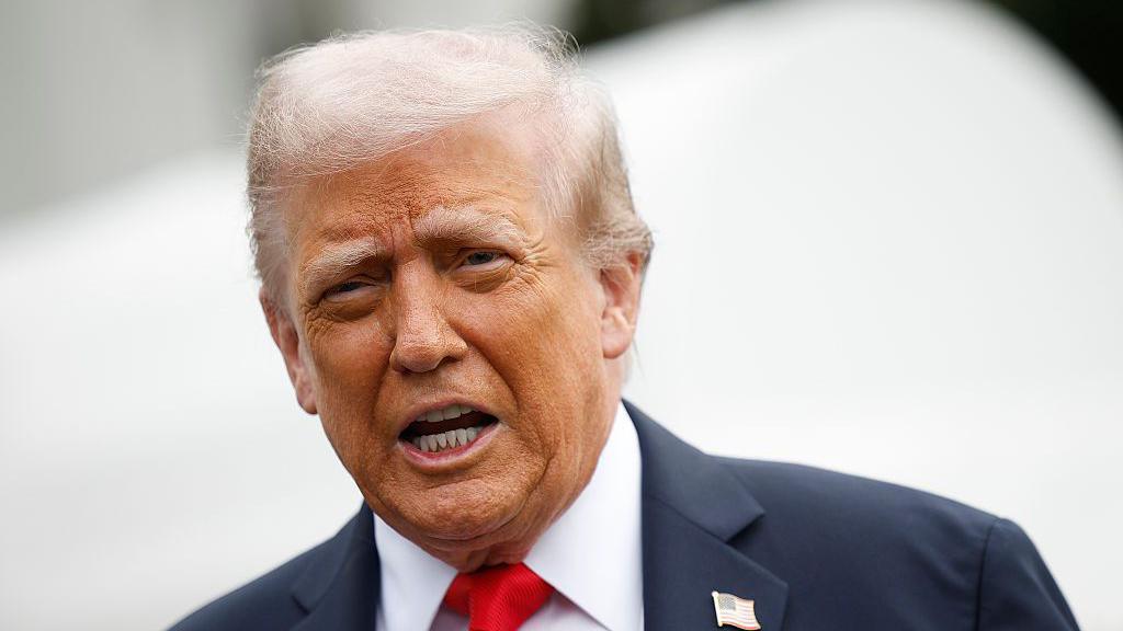 Donald Trump, mouth open as he's speaking, wearing dark suit an red tie