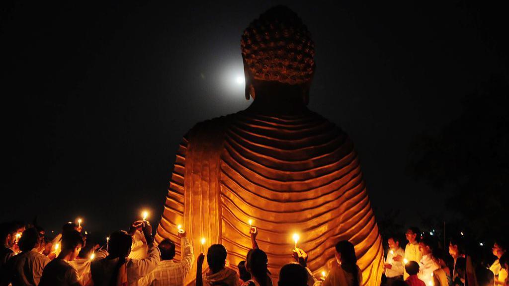 Buddhists celebrating Vesak observe the full moon behind a large statue of Buddha.