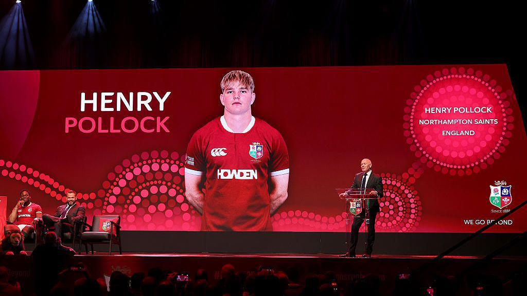A picture of Henry Pollock on a big screen in a Lions top with a podium in front