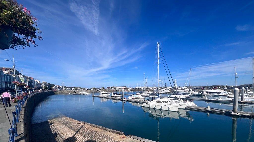 A harbour with pontoons full of boats on a sunny day. A granite slipway and blue iron railings to one site