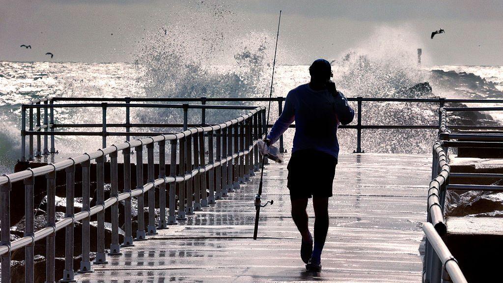 A fisherman walks on a decked area by the sea in Florida, as waves crash nearby