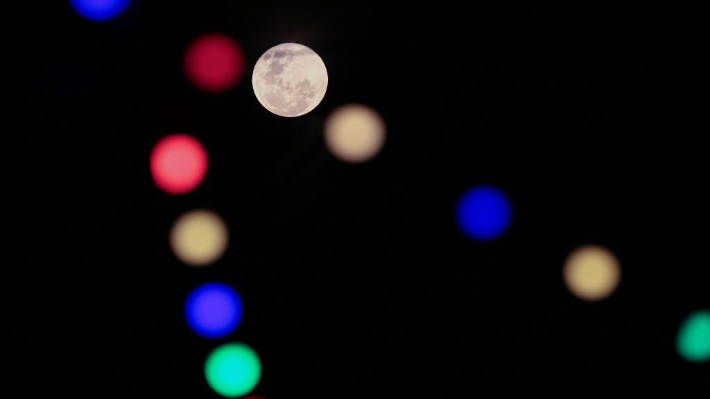 A view of the Moon aligned with the colorful lights of a restaurant in the coastal area of Puerto Madero, in Buenos Aires, Argentina,