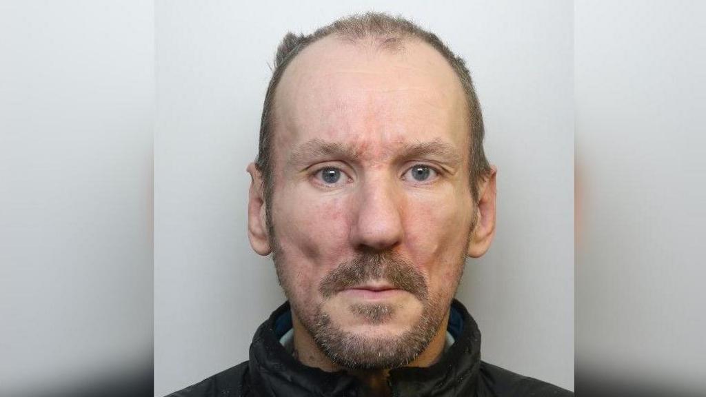 A mugshot of Alan Clune who is wearing a black fleece. He has brown hair and stuble.