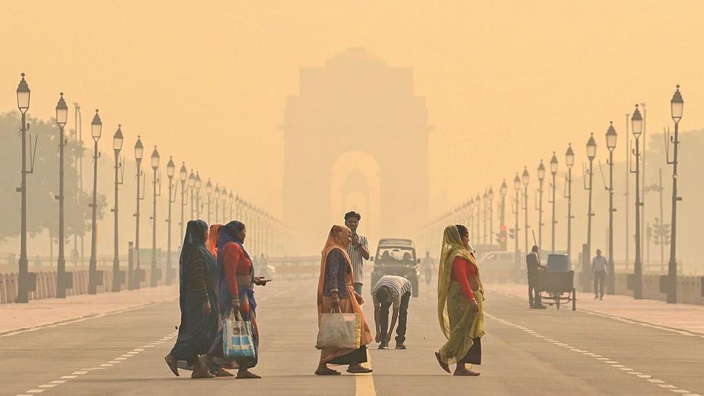 People cross the Kartavya Path, near India Gate in Delhi, with the area engulfed in a thick layer of smog in the morning mist of 27 October.