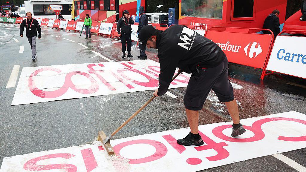 Vuelta staff brush hail off the surface at the finish line