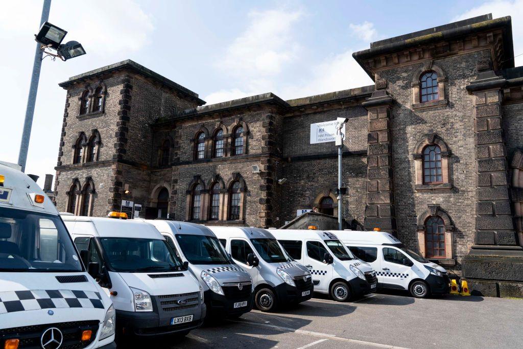 A general view of a Serco vehicle at Wandsworth prison in London. It is an imposing building with a gatehouse and what looks like a portcullis. A row of prison vans are by the entrance