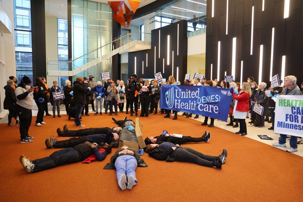 Protesters with People's Action lay in circle at health insurance giant UnitedHealth Group's headquarters holding signs saying "UnitedHealth denies care"