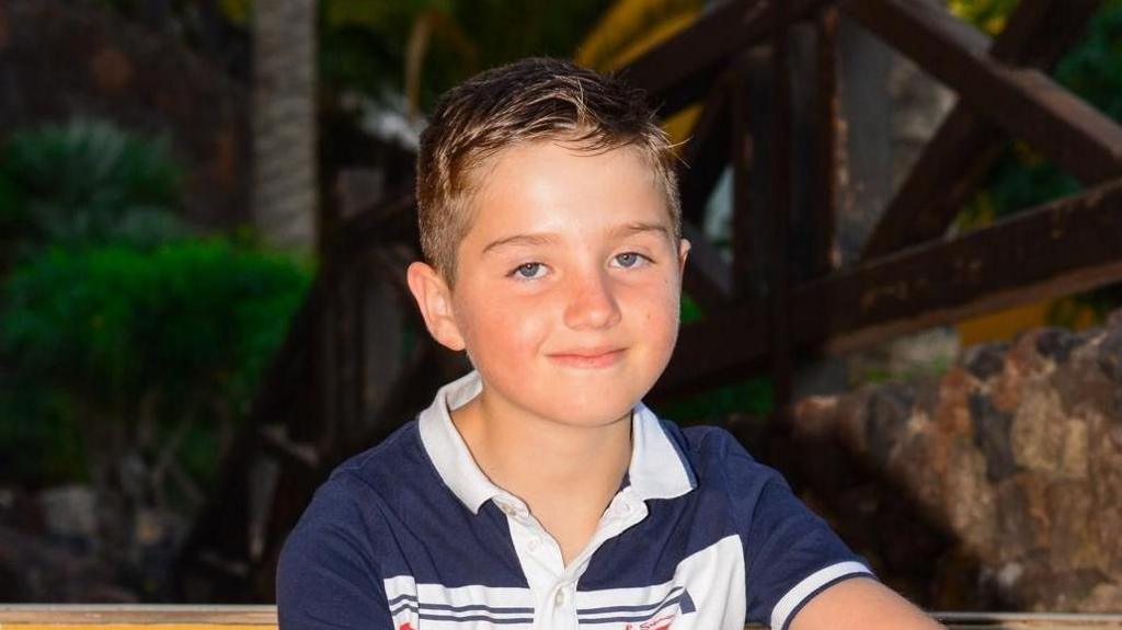 A young boy with short dark hair and wearing a navy and white polo shirt smiling into the camera. 