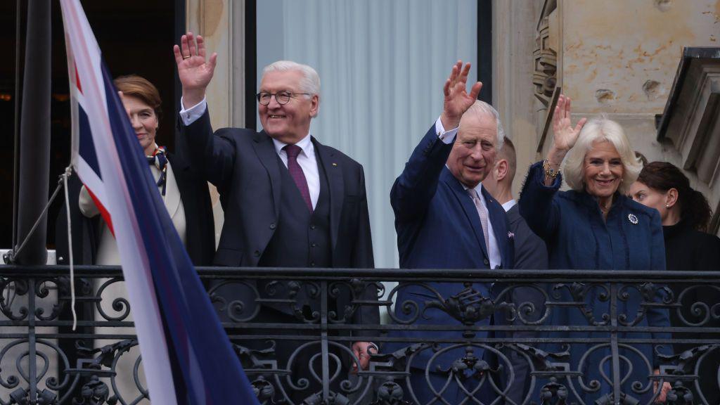 German President Frank-Walter Steinmeier (Centre Left), First Lady Elke Buedenbender (Left), King Charles III and Camilla, Queen Consort, greet crowds from a balcony.