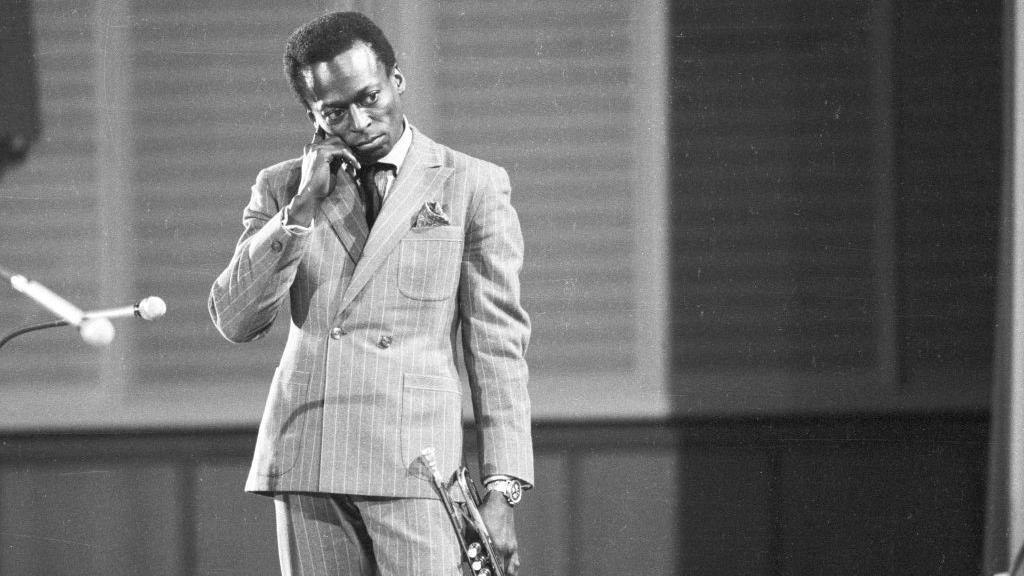 Miles Davis stands with his trumpet.