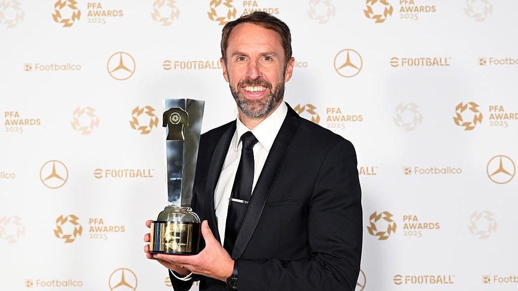 A man holds a long trophy and smiles