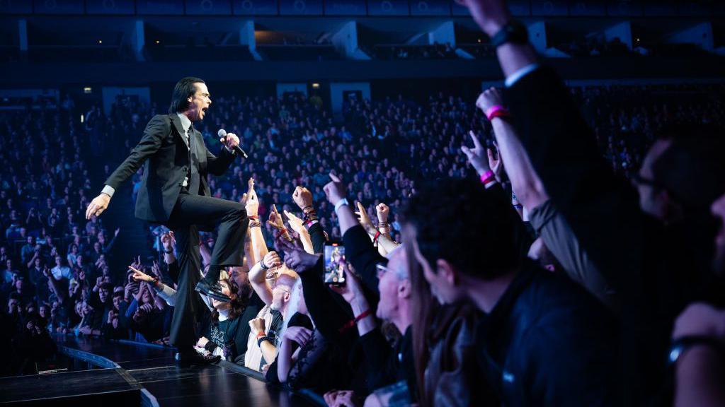 A musician performs on stage to a cheering crowd.