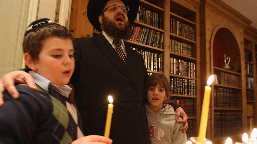 Two children and an adult light Hanukkah candles