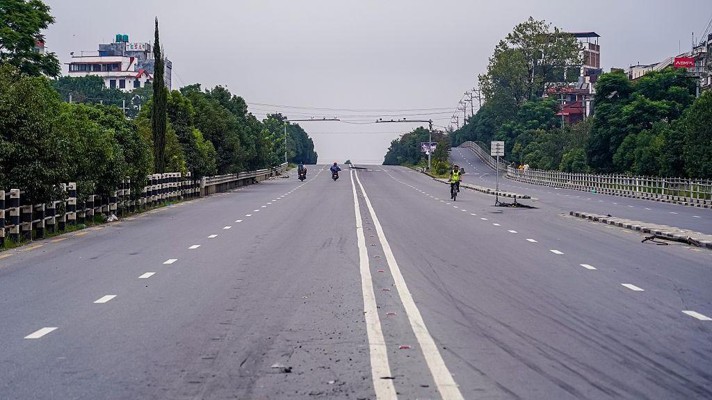 A wide, empty street with no protestors and only three people commuting on motorbikes.