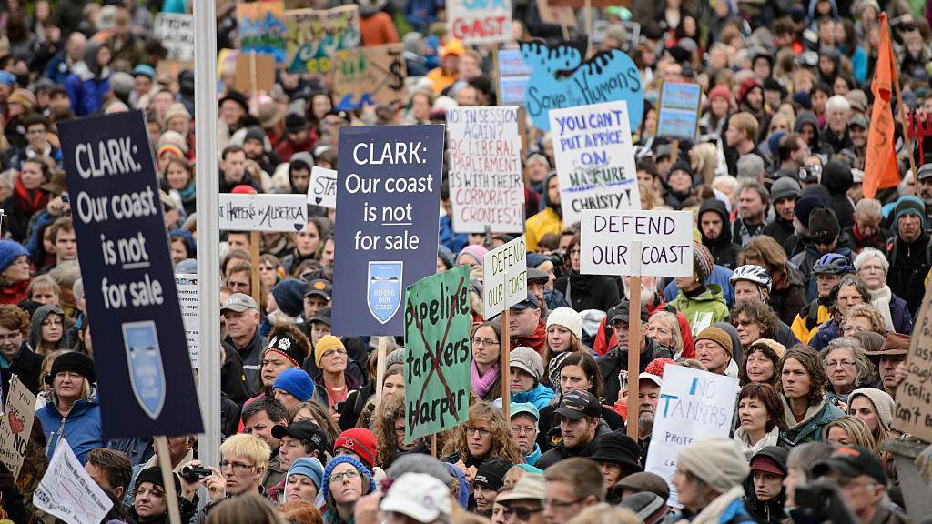 Protestors demonstrating against the proposed XL-Northern Gateway pipeline project, at the British Columbia Legislature building in Victoria. The pipeline would bring crude oil from the Alberta tar sands through British Columbia to the pacific coast. The image shows hundreds of people holding signs that say "Defend our Coast" "Our Coast is not for Sale" and "You can't put a price on nature"