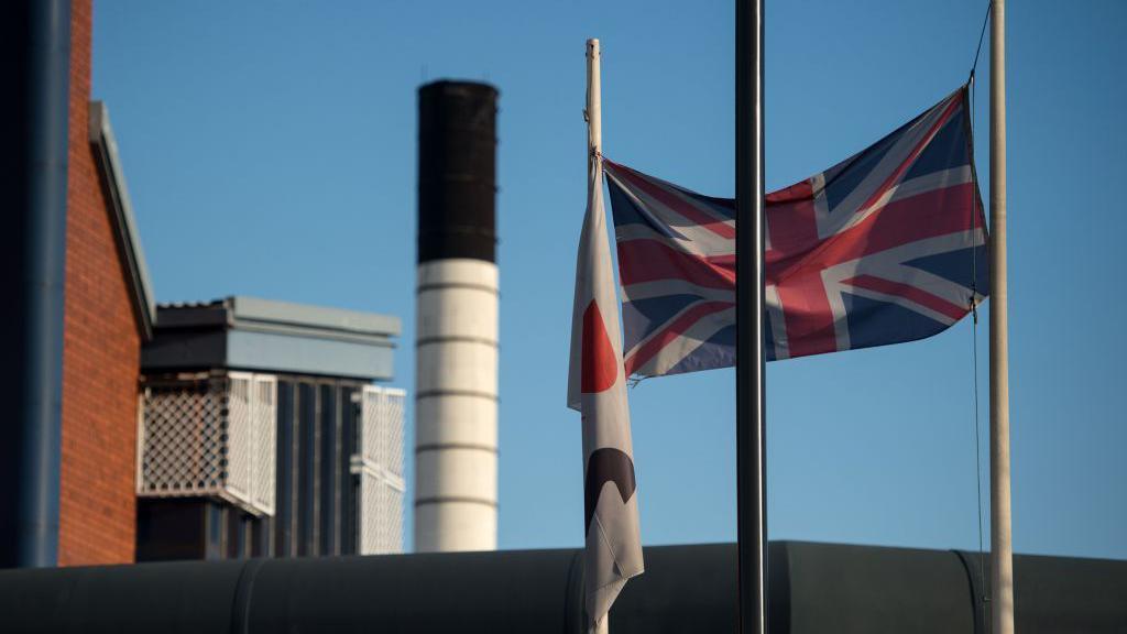 A prison with a union flag flying high. We can see some of the blocks behind. It is a clear and sunny day. The sky is blue.