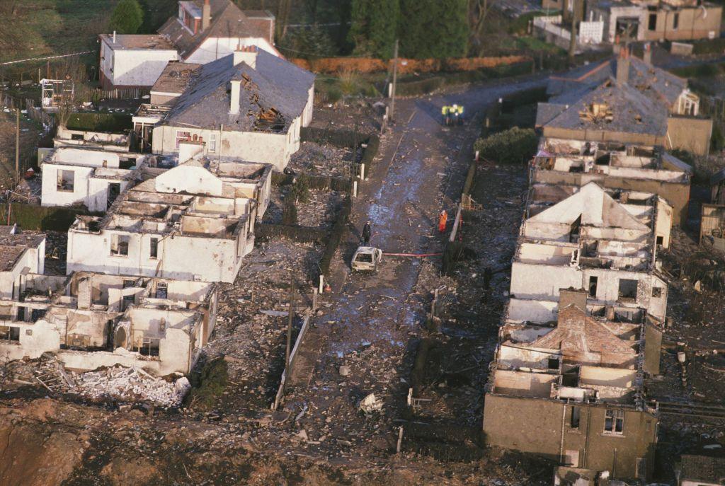 Sherwood Crescent in Lockerbie. A street of houses lies destroyed by the impact and fire of the crashed plane. Most of the houses have no roofs. There is debris everywhere.
