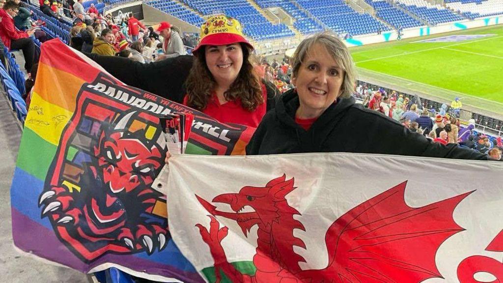 Judy Shaw (left) pictured at a football game holding up the Wales flag along with her daughter Holly. 