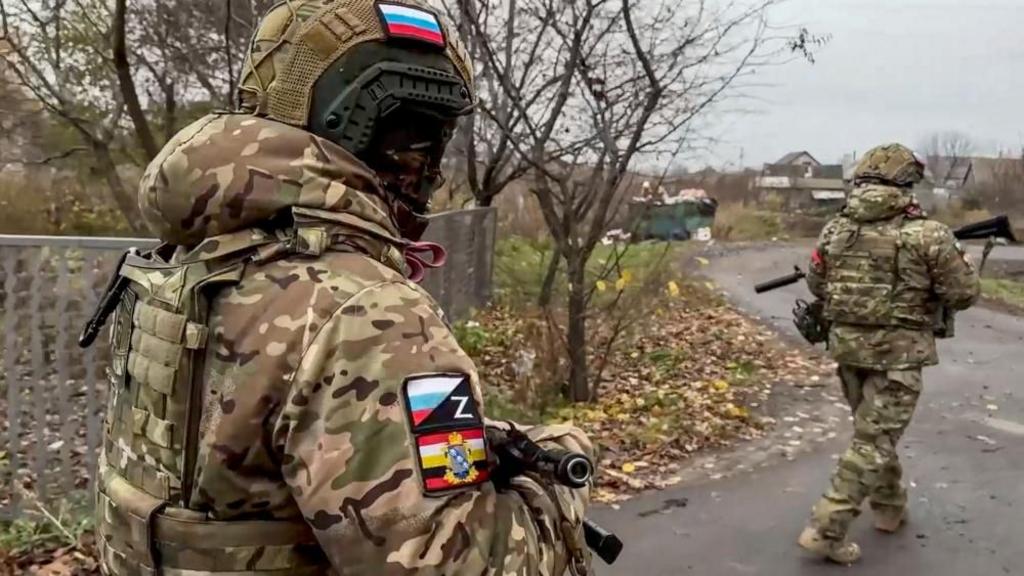 Russian military volunteers in uniform walking away from camera holding guns on residential street