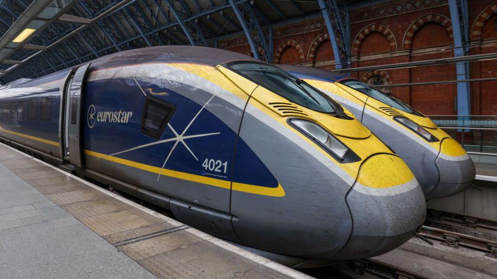 Two blue, grey and yellow Eurostar trains next to each other on a platform