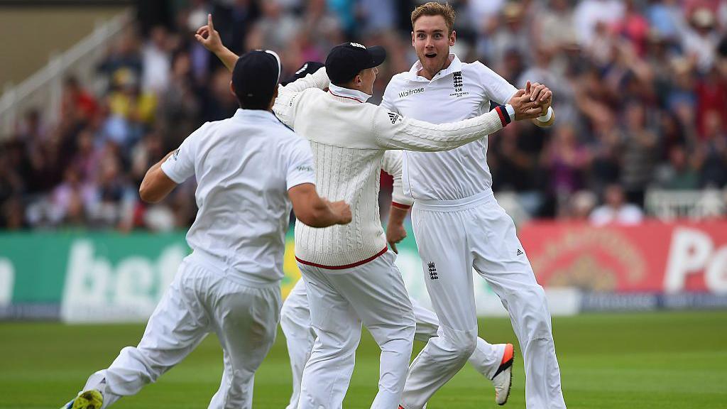 England players in white rush to embrace a surprised looking Stuart Broad in front of crowded stands at Trent Bridge