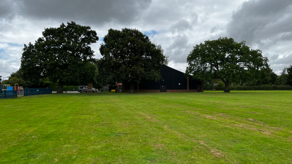 Three oak trees stand in a field next to a village hall