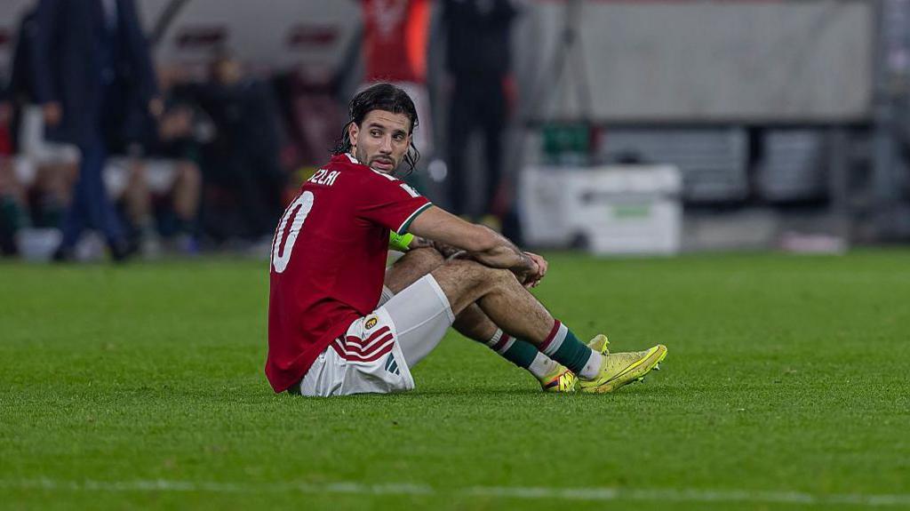 An emotional Dominik Szoboszlai sitting on the pitch