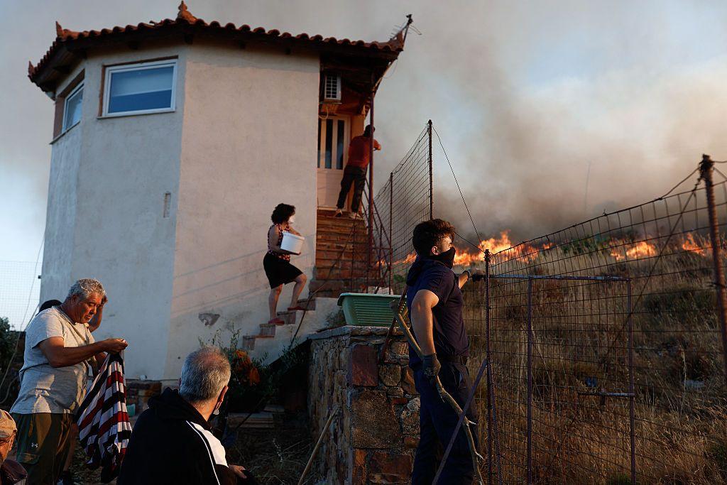 Residents try to contain a wildfire near a small building outside the town of Chios island in Greece, June 22, 2025. One lady is holding a bucket of water.