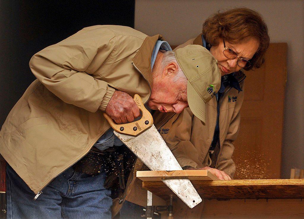 Carter and Rosalynn Carter cut a piece of wood with a saw