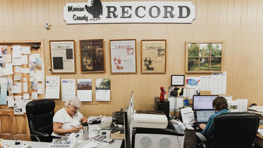  A volunteer acts as a receptionist for the Marion County Record while a reporter works on a story in Marion, Kansas. 