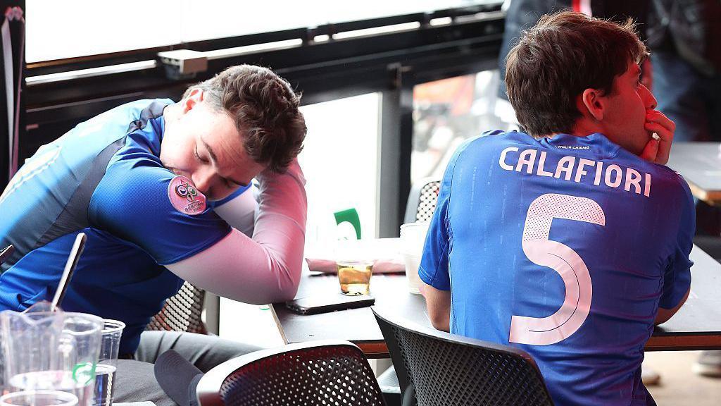 Italian football fans sit at a table and cover their faces