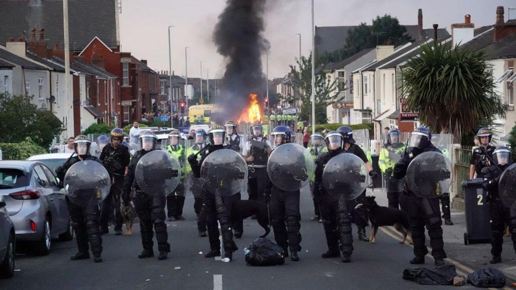 Riot police hold back protesters near a burning police vehicle after disorder broke out on July 30, 2024 in Southport, England.