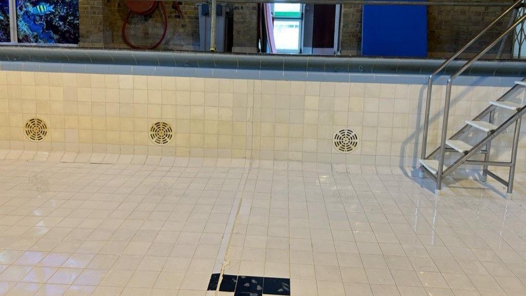 An image of the Ward Freman Swimming Pool with no water in it. It has cream tiles and metal steps.