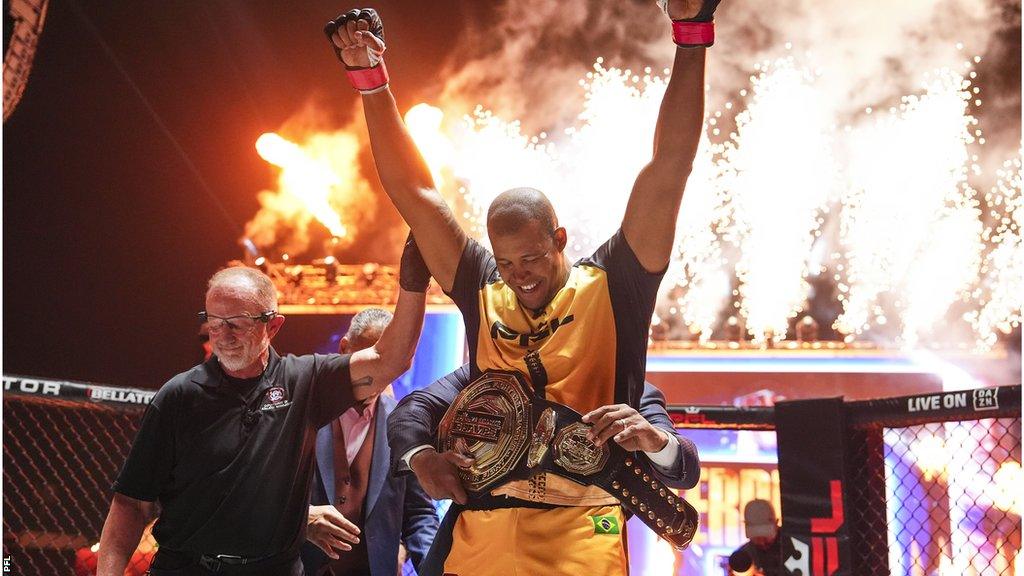 Renan Ferreira celebrates with a belt around his waist and fireworks in the background