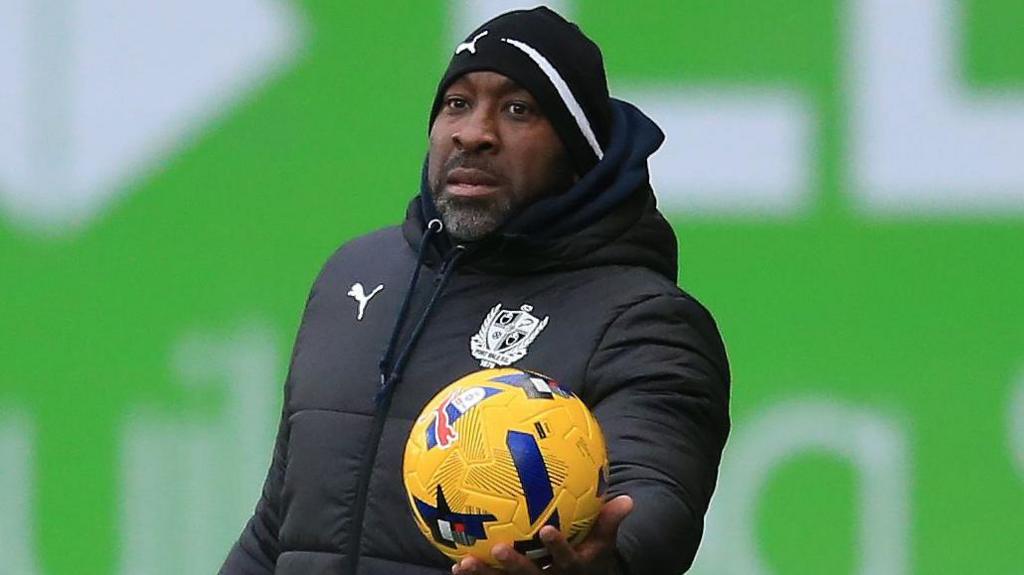 Port Vale manager Darren Moore holds the ball out in his left hand for a player to take a throw in during a match