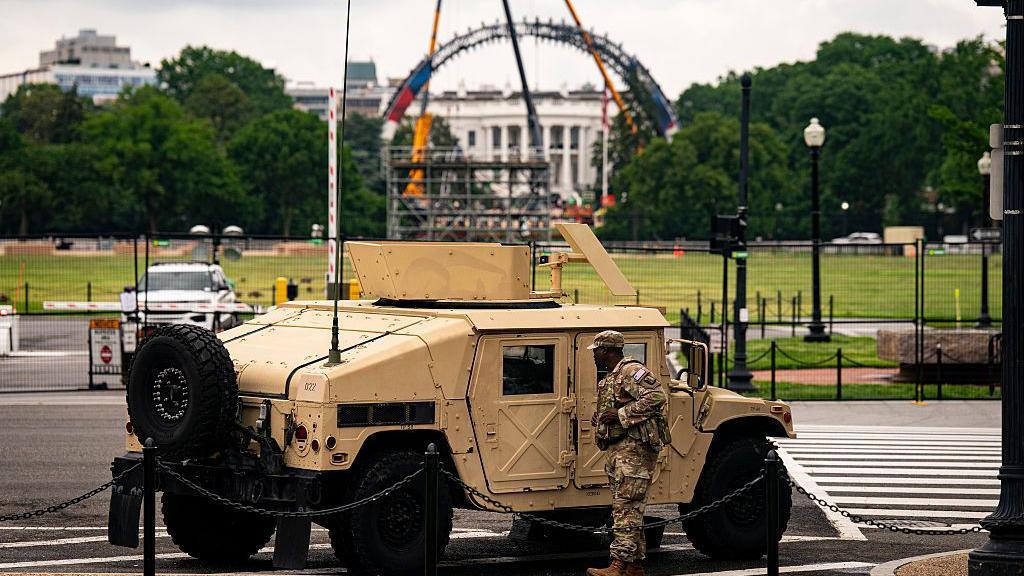 A member of the US National Guard stands next to an armoured vehicle with the White House in the background