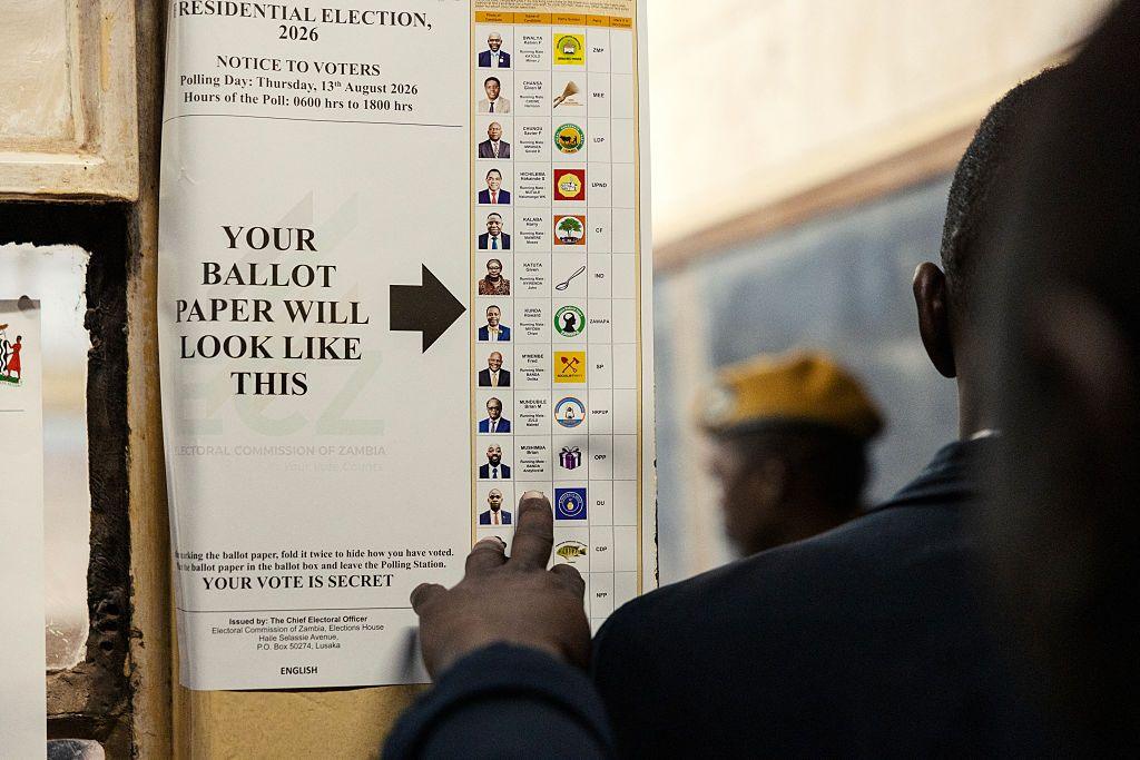 A specimen ballot paper is fixed to the wall. The back of a person's head can be seen as they look at the choice on offer.