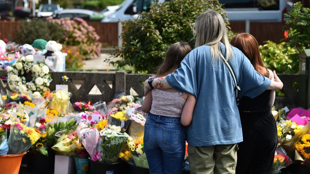 People look at floral tributes for the victims of the deadly knife attack in Southport last July 