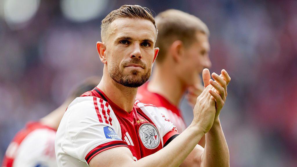 Jordan Henderson, wearing an Ajax shirt, looks out of shot and applauds