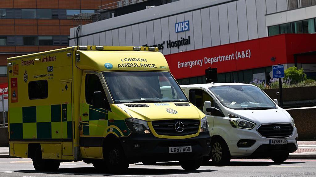 Yellow London Ambulance Service ambulance parked outside an NHS hospital emergency department (A&E).