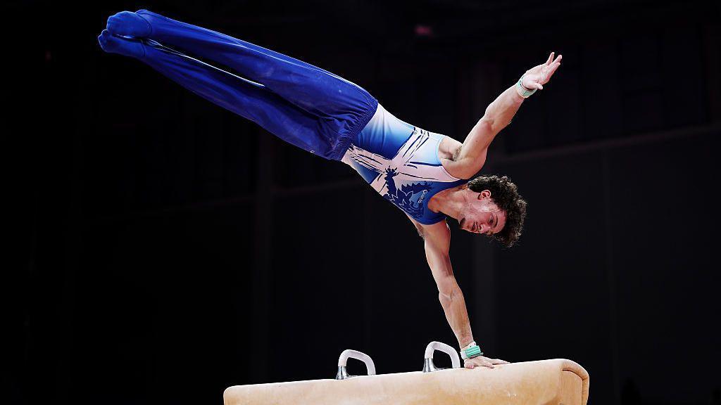Reuben Ward of Team Scotland competes in Pommel Horse. He is wearing bright blue and has curly brown hair.