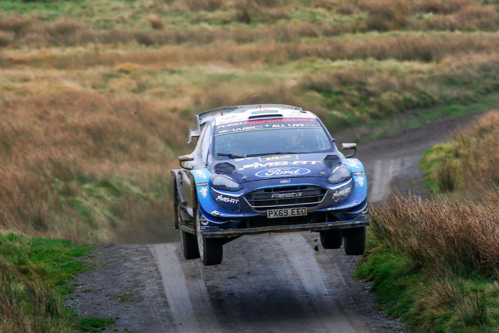 A blue world rally car with all four wheels off the ground as it moves at speed over a crest on a rally stage 